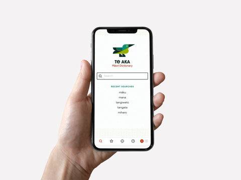 A hand holding a smartphone with the Māori Dictionary App on the screen Te Aka
