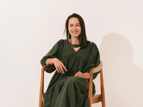 Māori woman in green dress sitting confidently in a wooden chair, smiling gently at the camera.
