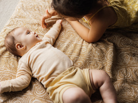 maori-baby-smiling-at-sibling-lying-on-mat
