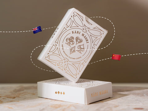 Kāri Māori playing cards box with NZ and China flags, symbolising the move from Aotearoa design to offshore production.