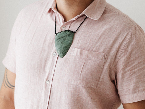 Man wearing a pink shirt with a large greenstone pounamu necklace.