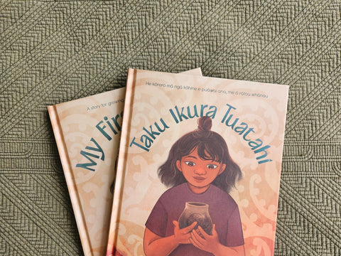 Two books titled 'My First Ikura' and 'Taku Ikura Tuatahi' by Qiane Matata-Sipu on a textured earthy green surface with Māori patterns
