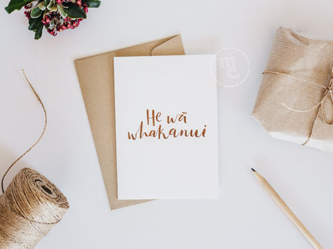 Hand-lettered Māori greeting card 'He wā whakanui' with a metallic gold envelope and natural wrapping materials.