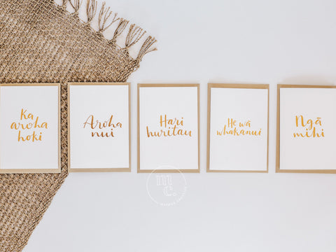 Collection of premium Māori greeting cards with gold foil text displayed on a natural fibre mat.
