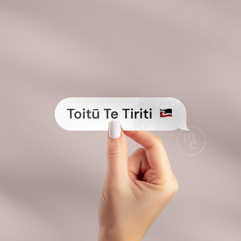 hand holding 'Toitū Te Tiriti' Māori vinyl decal sticker on a plain background, showcasing the phrase and Māori Tino Rangatiratanga flag