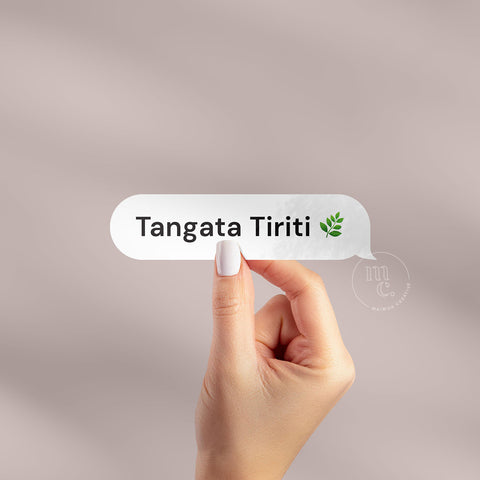Hand holding 'Tangata Tiriti' Māori vinyl sticker decal on a plain background, showcasing the phrase and a leaf emoji