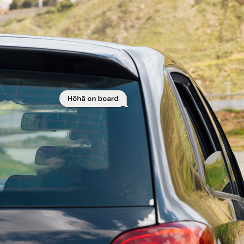 "Hōhā on board" Māori bumper sticker vinyl decal on a car window, set against a scenic outdoor backdrop