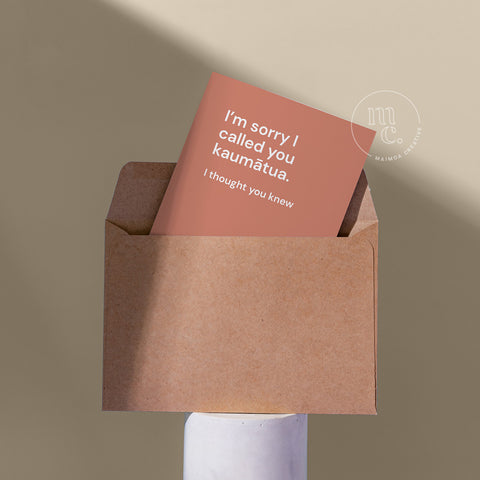 Cheeky card peeping from a kraft envelope on a plinth with the text "I’m sorry I called you kaumātua. I thought you knew," against a beige background.