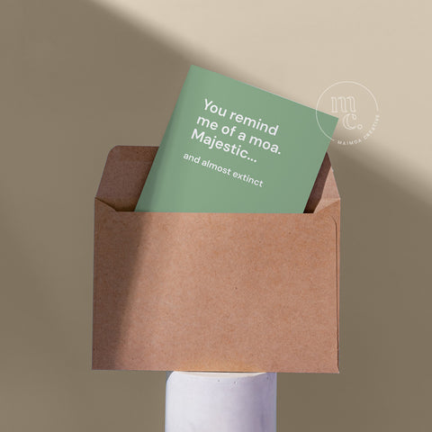Cheeky card peeping from a kraft envelope on a plinth with the text 'You remind me of a moa. Majestic...and almost extinct' against a beige background.