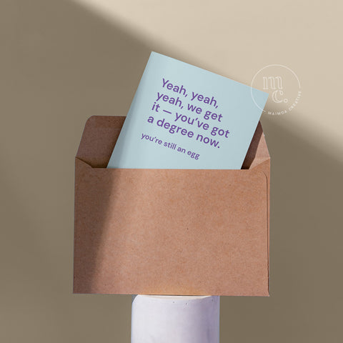 Cheeky card peeping from a kraft envelope on a plinth with the text 'Yeah, yeah, yeah, we get it — you’ve got a degree now. You're still an egg,' against a beige background.