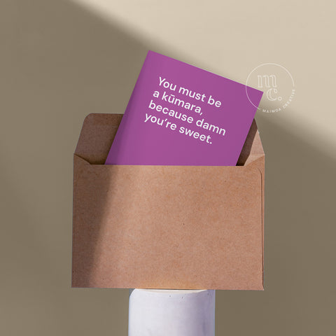 Cute card peeping from a kraft envelope on a plinth with the text ''You must be a kūmara, because damn you’re sweet'.' against a beige background.