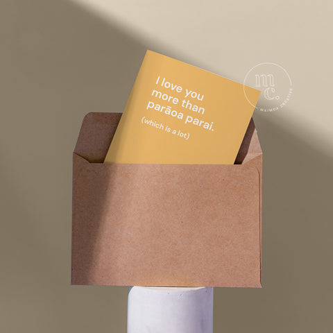Cute card peeping from a kraft envelope on a plinth with the text 'I love you more than parāoa parai.' against a beige background.