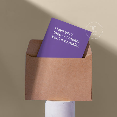 Cheeky card peeping from a kraft envelope on a plinth with the text 'I love your teke — I mean, you’re tu meke' against a beige background.