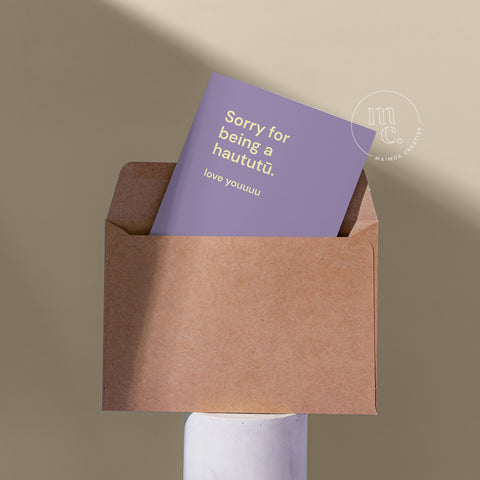 Cheeky card peeping from a kraft envelope on a plinth with the text 'Sorry for being a haututū. love youuuu,' against a beige background.