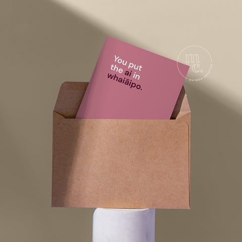 R18 card peeping from a kraft envelope on a plinth with the text 'You put the ai in whaiāipo' against a beige background.