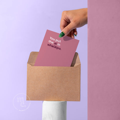 R18 card being pulled by a hand from a kraft envelope on a plinth with the text 'You put the ai in whaiāipo' against a pastel purple background.