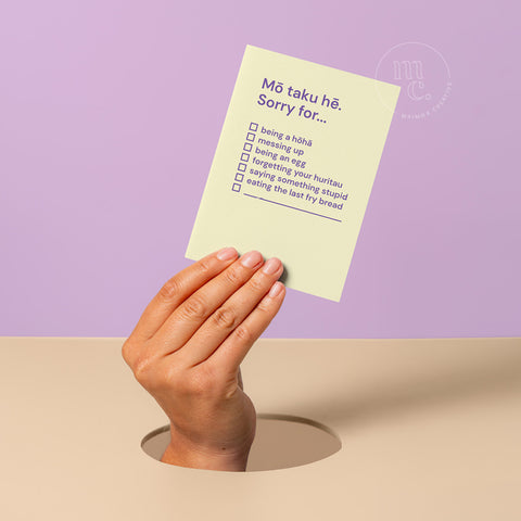 Hand emerging from a hole holding a humorous Māori apology card that says “Mō taku hē. Sorry for…” with checklist options, by Maimoa Creative.