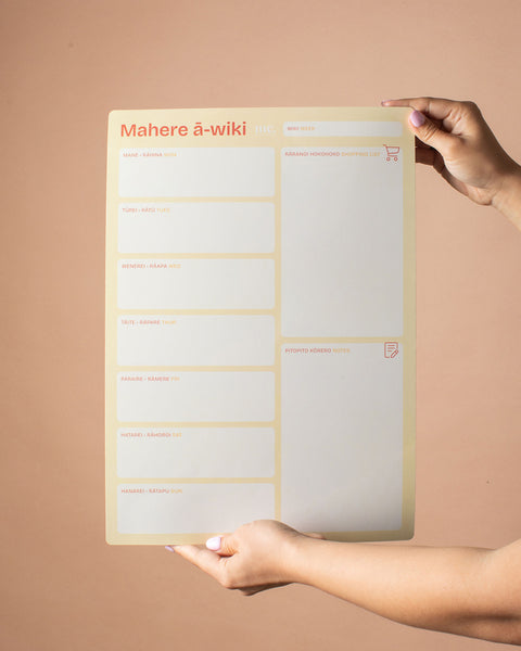 Person holding a magnetic weekly planner with 'Mahere ā-wiki' title against a beige background