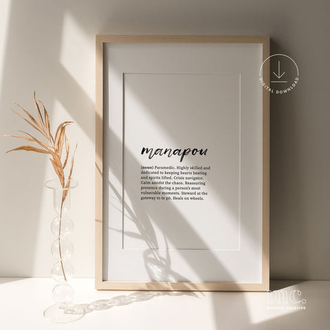 Framed 'manapou' definition print illuminated by sunlight, next to a delicate dried plant arrangement