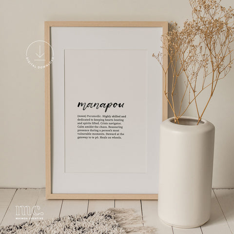 Framed 'manapou' definition print next to a white vase with dried plants on a wooden floor.