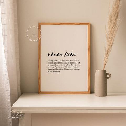 Modern home setting featuring a framed 'Whaea Kēkē' print on a white console table, accented by a minimalist ceramic vase and dried grass.