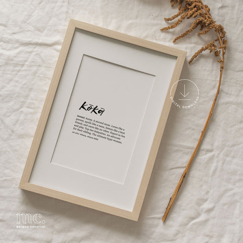 Framed 'Kōkā' print laid on a textured linen background, complemented by dried botanicals to the side.