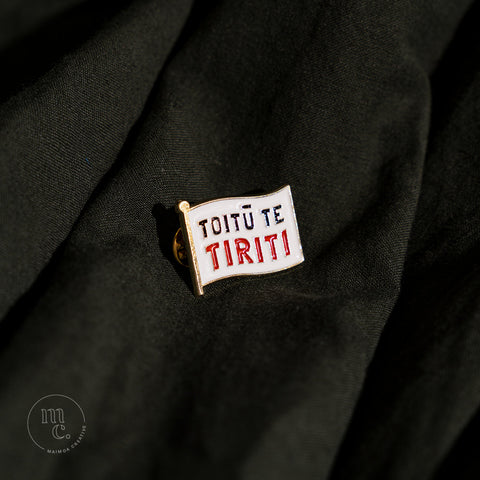  An enamel badge pin with the words "Toitū te Tiriti" written in bold letters on dark forest green material