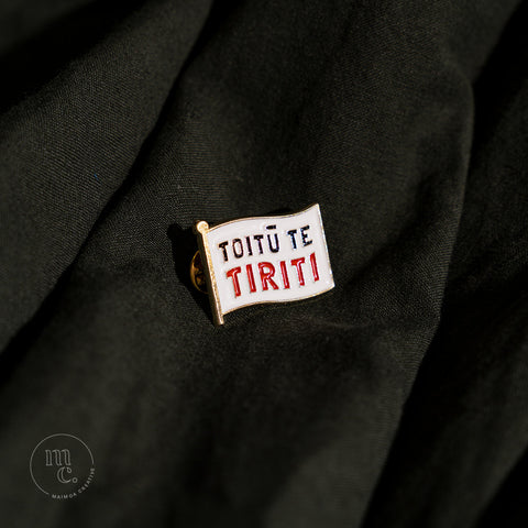 An enamel badge pin with the words "Toitū te Tiriti" written in bold letters on dark forest green material