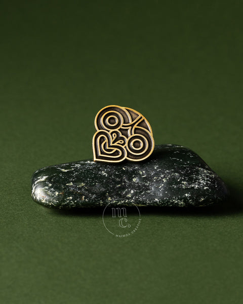 Gold decorative tiki pin on a dark greenstone pounamu with a green background