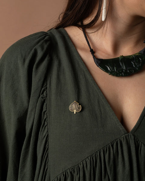 Person wearing a dark green dress with a decorative kawakawa leaf brooch