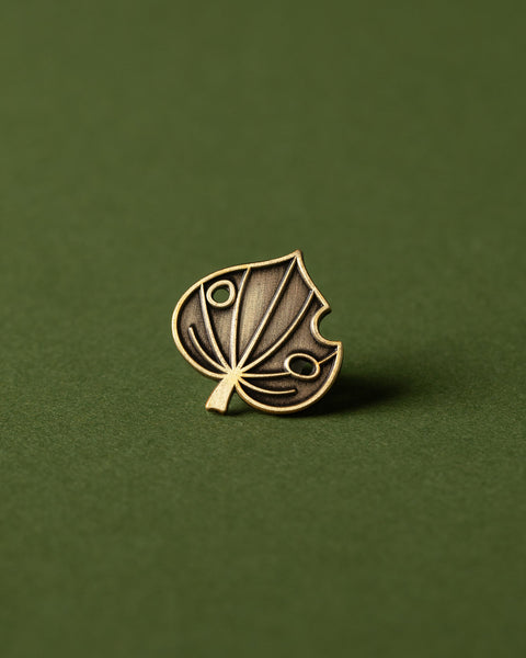 Antique gold kawakawa leaf brooch pin on a green background