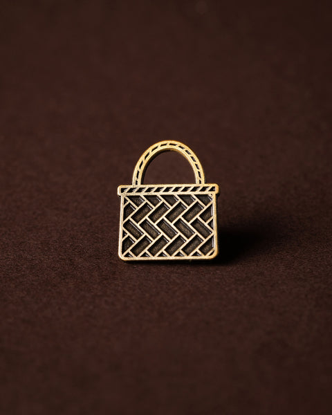 Gold woven kete basket pin on a brown background