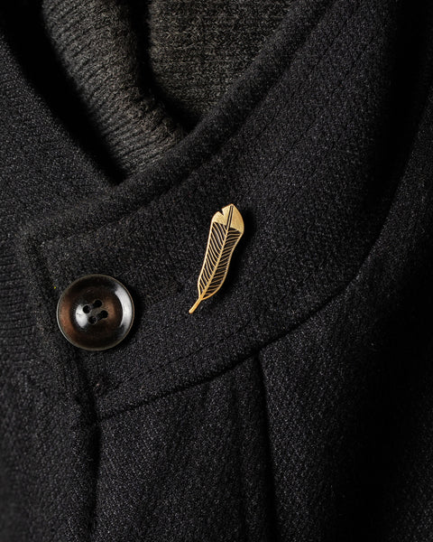 Gold huia feather pin on a dark coat collar with a button