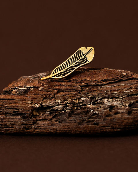 Gold huia feather brooch on a wooden surface with a brown background