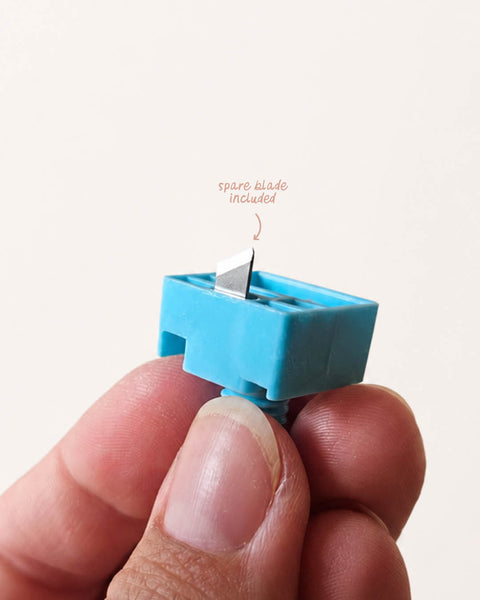 Blue blade holder for circle cutter, held between fingers against a light background.