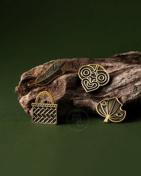 Gold Māori pins on a wooden surface with a green background