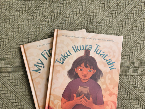 Two books titled 'My First Ikura' and 'Taku Ikura Tuatahi' by Qiane Matata-Sipu on a textured earthy green surface with Māori patterns