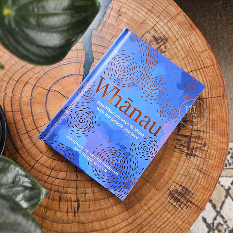 Whānau book cover – illustrated reo Māori phrases by Donovan Farnham and Rehua Wilson, styled on wooden table and plant.