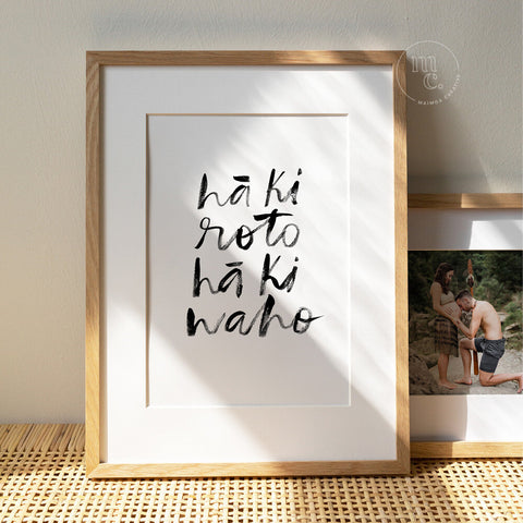 Framed Māori art print featuring hand-lettered text “Hā ki roto, hā ki waho” displayed in a sunlit, natural home setting.