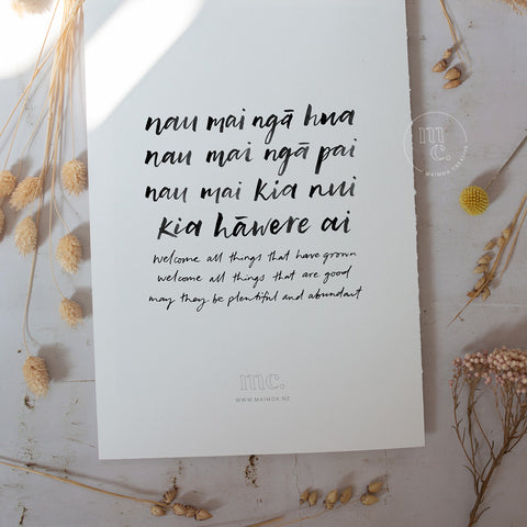 Māori blessing print "Nau mai ngā hua" displayed with dried flora on a textured surface, conveying a message of welcome and abundance.