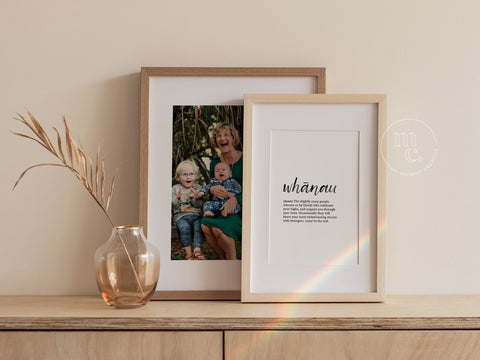 Two framed prints on a wooden sideboard; one with a 'whānau' definition, the other showing a grandmother with two children.