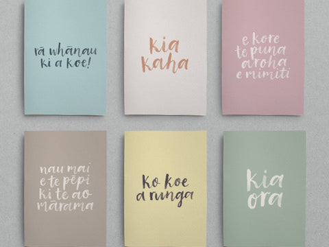 Six Māori greeting cards in various pastel colours with phrases 'rā whānau ki a koe', 'kia kaha', 'e kore te puna aroha e mimiti', 'nau mai e te pēpi ki te ao mārama', 'ko koe a runga', and 'kia ora' written in hand lettered font