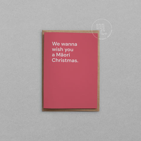 Greeting card with text 'We wanna wish you a Māori Christmas' on a bright red background, placed on a light surface