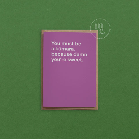 Greeting card with text 'You must be a kūmara, because damn you’re sweet.' on a bright purple background, placed on a contrasting surface