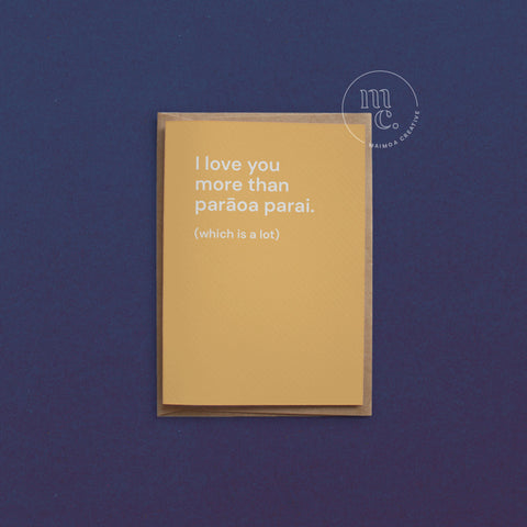 Greeting card with text 'I love you more than parāoa parai. (which is a lot)' on a bright yellow background, placed on a contrasting surface