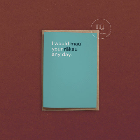 Greeting card with text 'I would mau your rākau any day.' on a bright teal background, placed on a contrasting surface