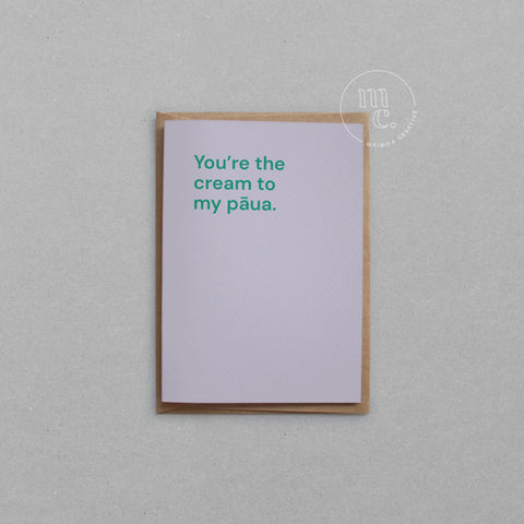 Greeting card with text 'You're the cream to my pāua' on a pastel purple background, placed on a light surface