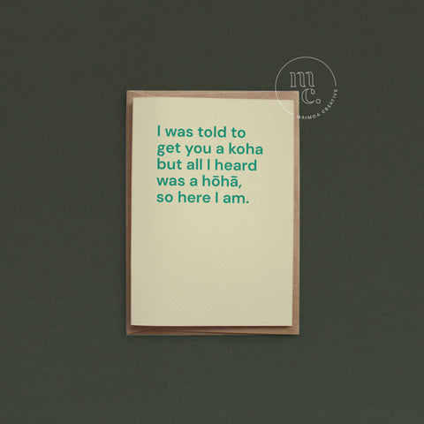 Greeting card with text 'I was told to get you a koha but all I heard was a hōhā, so here I am.' on a light yellow background, placed on a dark surface