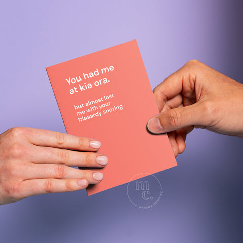 Two hands passing a card between themselves with the text 'You had me at kia ora. But almost lost me with your blaaaardy snoring,' and a light pastel purple background