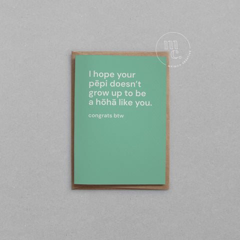 Greeting card with text 'I hope your pēpi doesn’t grow up to be a hōhā like you. congrats btw' on a mint green background, placed on a light surface